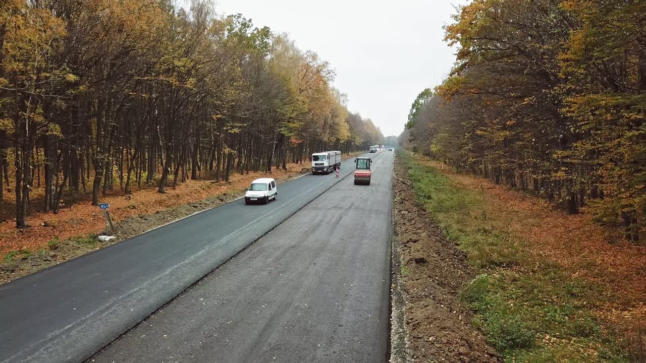 Cars moving on half of asphalt road in autumn. Road repair works on one side of the road at highway in the forest. Camera moves back.