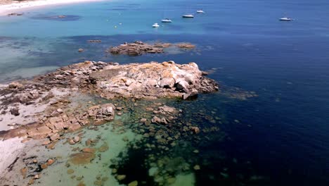 aerial orbital footage of rocky shore with clear and dark water and sailboats