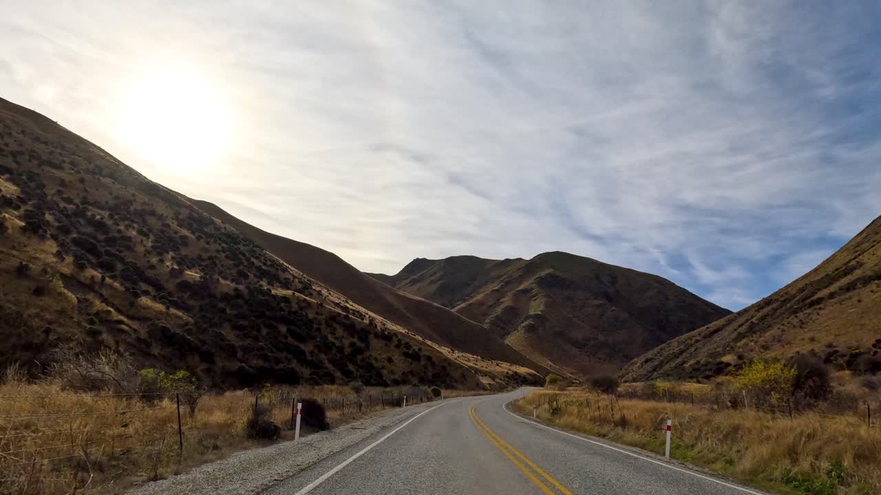 A serene drive through Queenstown's winding roads, surrounded by autumnal mountains under a bright sky. Captured in natural daylight