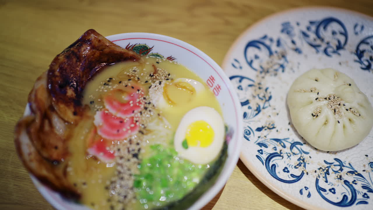 チャーシュー、半熟卵、麺、青菜、ごまが乗ったラーメン鉢と、隣に置かれた蒸しパン。