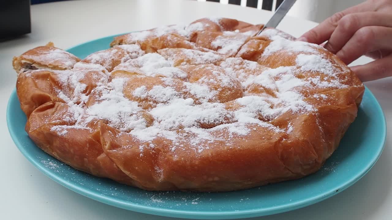 Freshly baked chocolate-filled ensaimada topped with powdered sugar on a blue plate