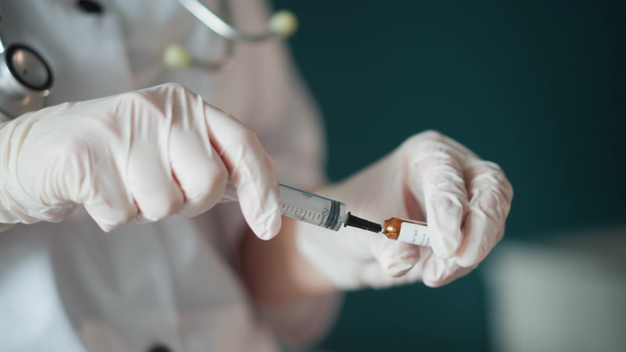 Il medico preleva il farmaco con attenzione. Il medico estrae con perizia il medicinale da una fiala ambrata durante la visita. Mani guantate preparano con cura la dose da un contenitore ambrato in un ambiente clinico.