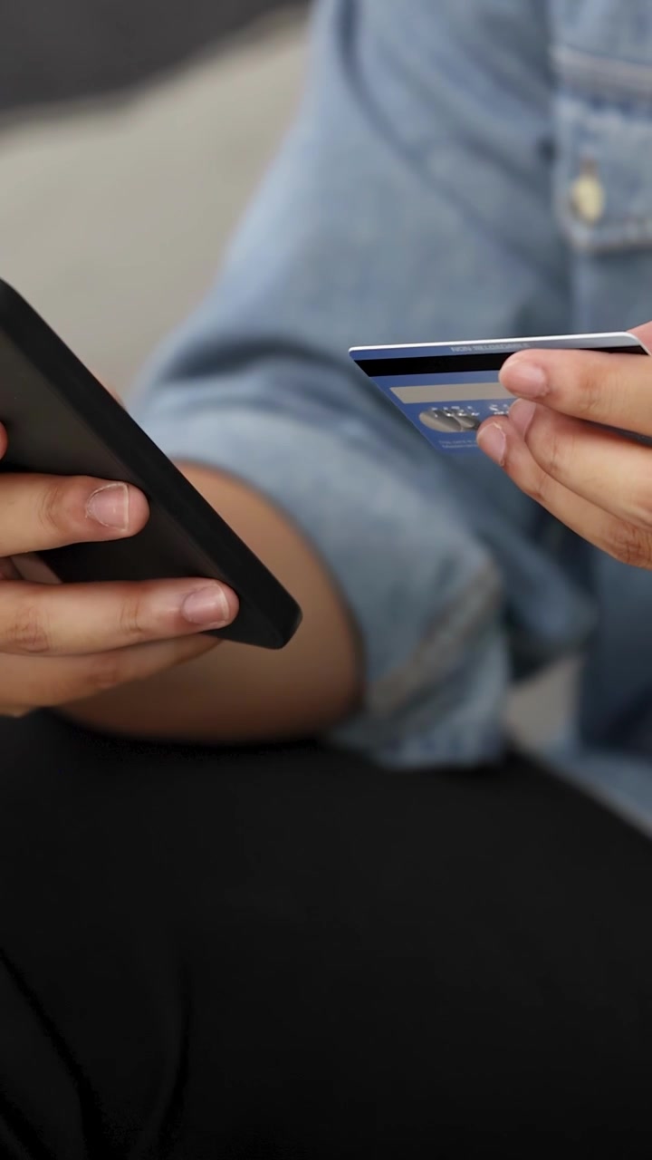 Primo piano di mani che tengono uno smartphone e una carta di credito mentre effettuano un acquisto online.