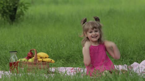 weekend at picnic. lovely caucasian child girl on green grass meadow sit on blanket waving her hands