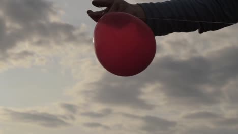 holding a red balloon against cloudscape