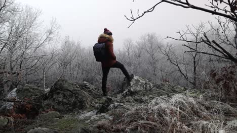 Caucasian-hiker-man-in-warm-brown-jacket-with-fluffy-hood-wandering-around-in-misty-frozen-forest