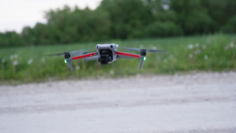 a compact quadcopter drone with glowing lights is ready for takeoff on a gravel surface, showcasing modern aerial technology and outdoor operation.