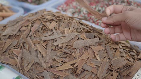 a hand picks up a piece of cinnamon from a pile of cinnamon sticks in a market