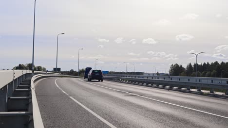 cars driving on a bridge or an overpass during a sunny day in laagri estonia. the bridge goes over pärnu highway. sun is shining and some clouds are in the sky. road has white markings and lamp posts.