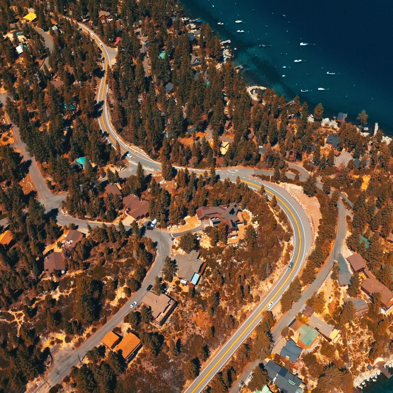 Sunlit wooded waterfront with private cottages among the trees. Amazingly deep blue waters of lake with numerous boats near the shore. Top view