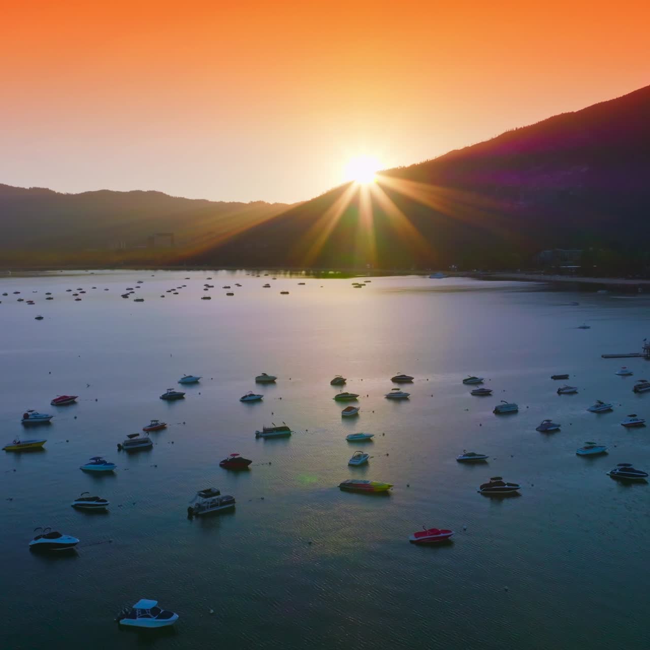 Bright orange sky over the Lake Tahoe at sunset. Numerous boats enjoying the sundown view from water. Aerial view
