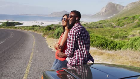 african american couple embracing each other while standing near convertible car on on road
