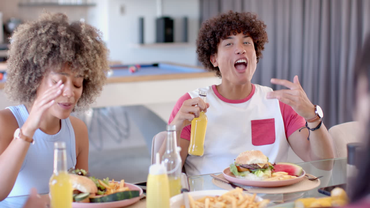 Diverse friends enjoying meal, eating burgers and drinking soda at table