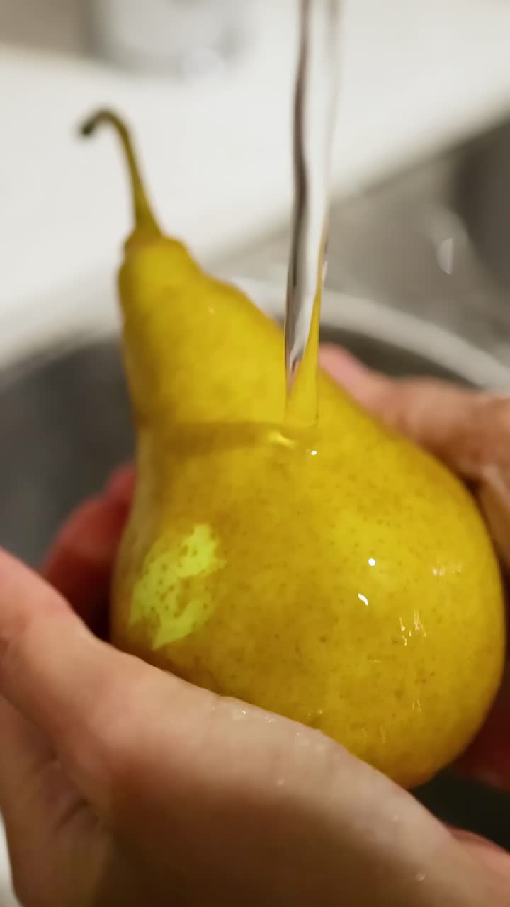 Manos lavando una pera bajo agua corriente