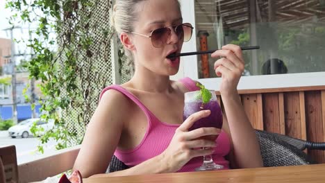 mujer disfrutando de un cóctel púrpura en un café al aire libre