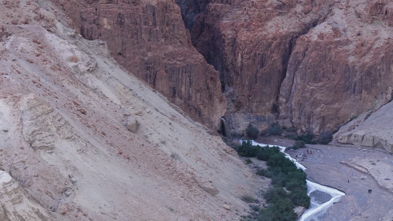 Ampia angolazione aerea da drone che mostra la portata di un'inondazione lampo che attraversa il profondo canyon del fiume Kidron nel deserto della Giudea, in Israele, con escursionisti visibili in lontananza.