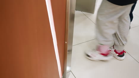 camera showing the lower half of various people walking into an elevator. the scene captures the movement and variety of footwear as individuals enter the elevator