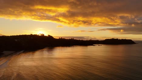 golden sunset with bright sunlight behind coastline of new zealand. aerial lateral wide shot. tranquil water of bay. mystic clouds at sky.