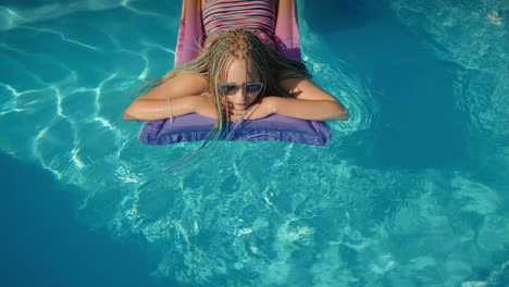 A-child-with-afro-pigtails-swims-on-an-inflatable-mattress-in-the-pool,-resting-and-enjoying-the-rest.-Top-view