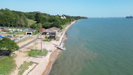 an aerial view captures the scenic beauty of fishbourne beach on the isle of wight, showcasing the sandy shore, clear blue waters, and lush greenery under a clear sky.