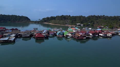 Bang Bao Pier floating village in Koh Chang island, Thailand, showing colorful houses and boats sailing in turquoise water. Fantastic aerial view flight dolly right drone