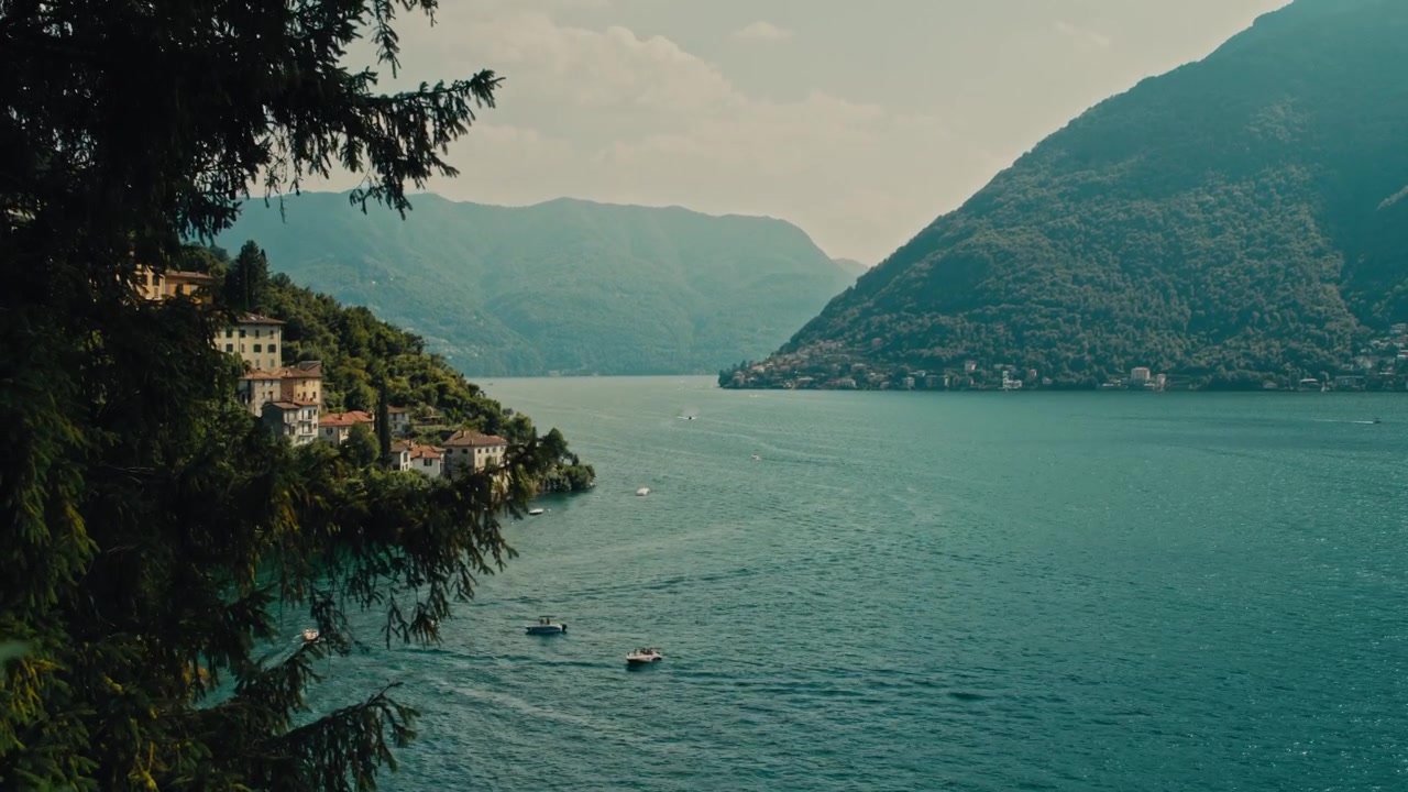Vista panoramica del Lago di Como con montagne, ville e barche sull'acqua.
