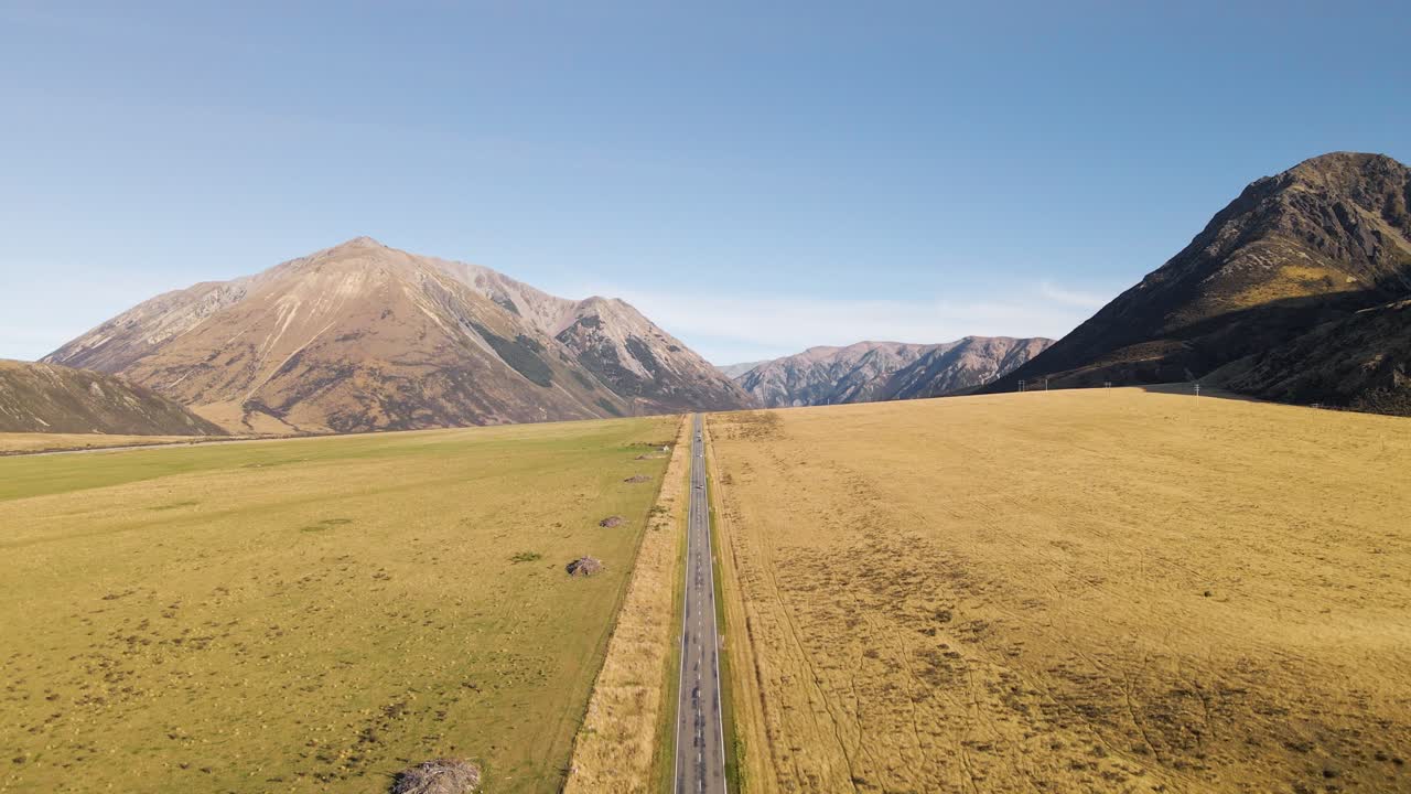 Straight road surrounded by rugged mountains and golden plains