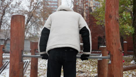 운동선수 는 야외 운동 장비 를 사용 하여 피트니스 를 하기 위해 장비 를 준비 하고 있으며, 배경 에는 눈 으로 인 나무 와 도시 건축물 들 이 둘러싸여 있다