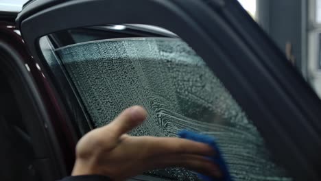 hand uses scrubbing pad in wiping car window with cleaning detergent at carwash