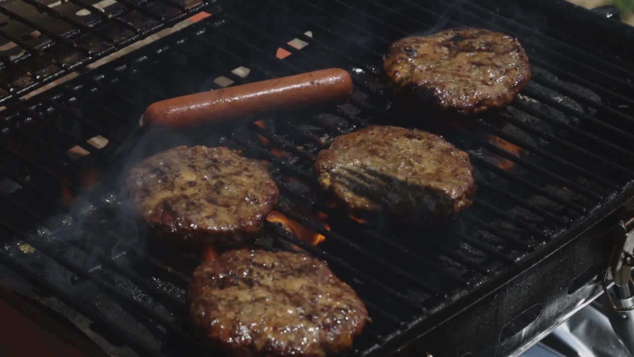Hamburger e hot dog grigliati sul fuoco a carbone sulla griglia - primo piano al rallentatore