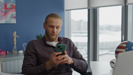 Smiling-student-typing-mobile-at-table-close-up.-Positive-man-resting-smartphone