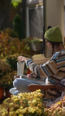 young woman drawing on a tablet while sitting in a camping chair outside a camper van