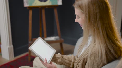 side view of young woman watching something on tablet while sitting on a couch at home