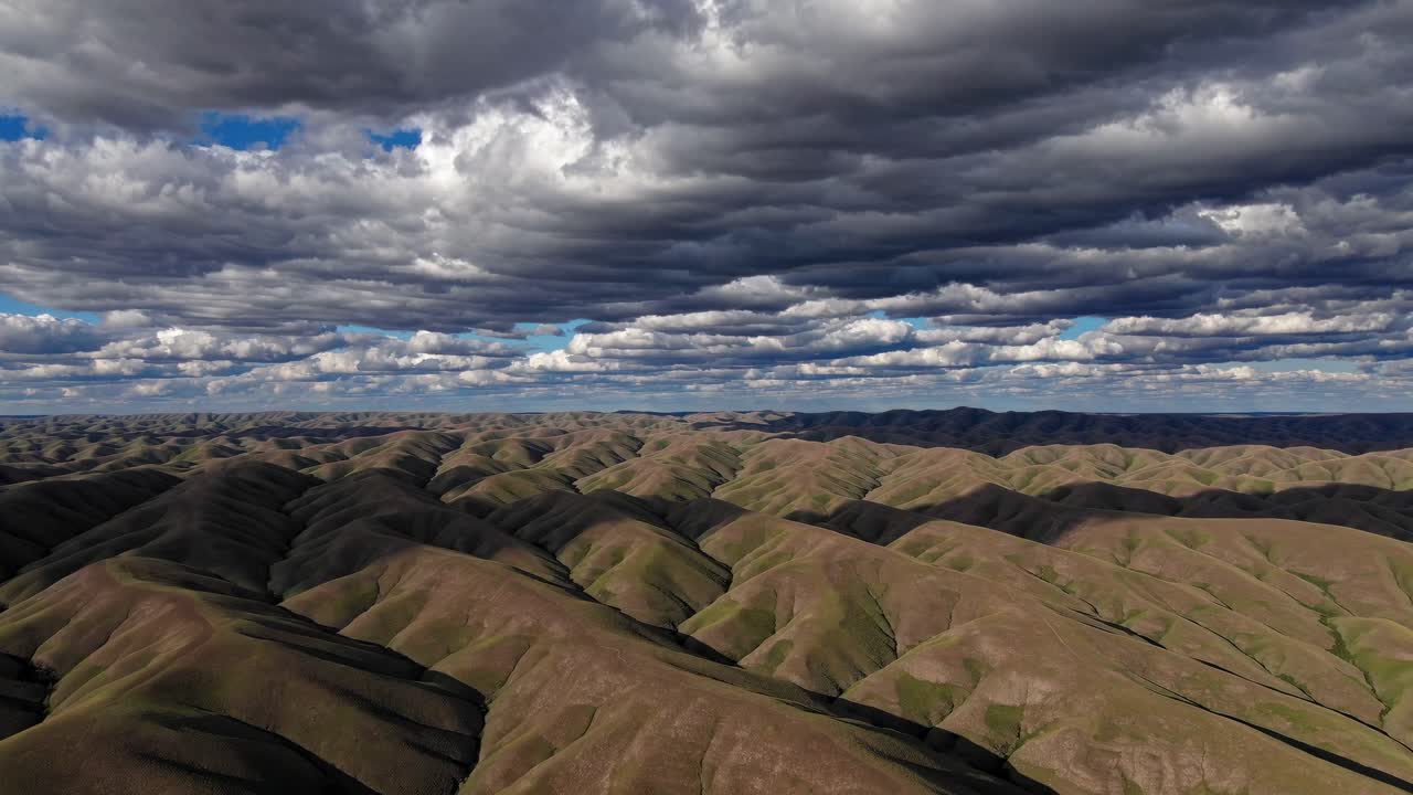 Aerial video captures rolling hills under dramatic, cloud-filled skies