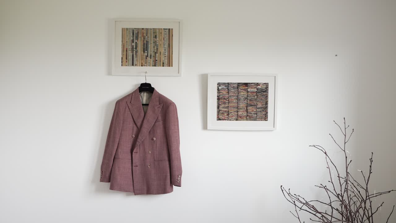 분홍색 슈트 재은 미니멀리즘 방에서 프레임 된 미술품으로 둘러싸인 벽에 끔하게 매달려 있습니다.