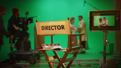 on film studio set focus on empty director's chair. in the background professional crew shooting historic movie, cameraman on railway trolley shooting green screen scene with actors for history movie