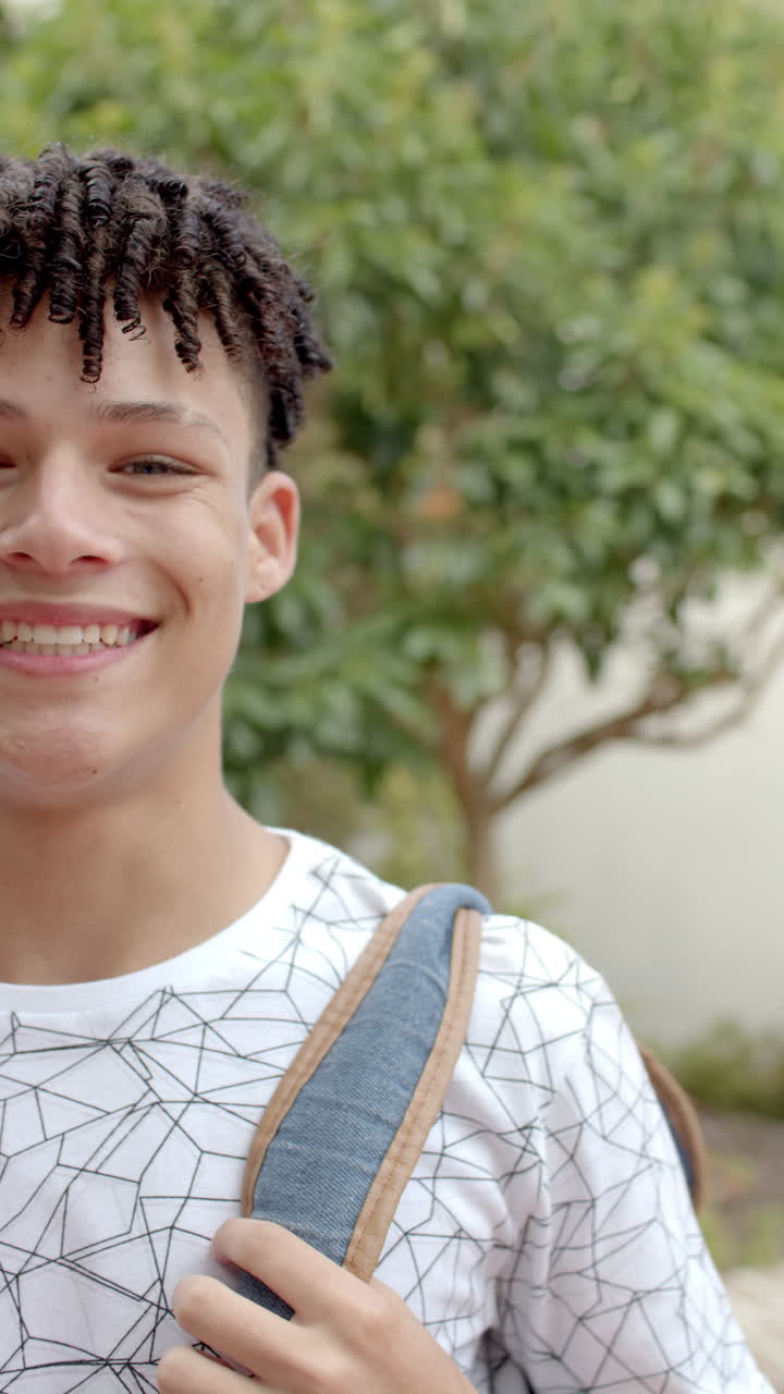 Vertical video: Standing outdoors, smiling teenager with backpack ready for school