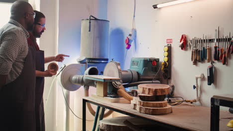 fabricante que enseña a un nuevo empleado cómo dar forma a un cuenco de madera en una lijadora de disco