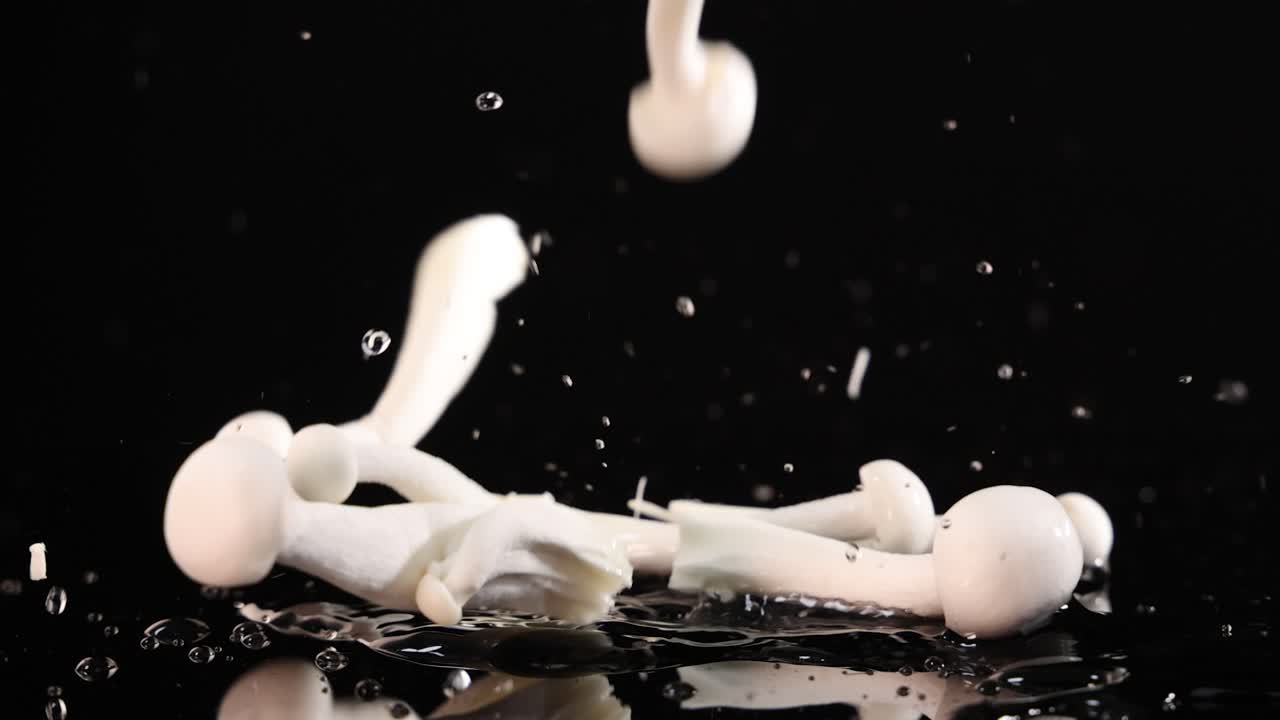 White beech mushrooms fall and scatter on a glossy black surface, captured in high-speed close-up with dramatic lighting and crisp detail