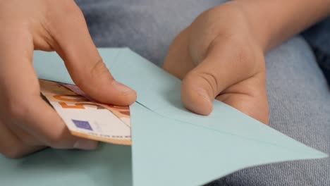 teenage boy hands open blue envelope, checking, counting a few cash euro banknotes. present gift, saving, financial literacy for children