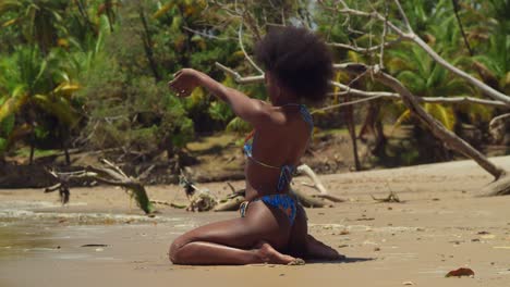 on a sunny day, a girl with curly hair in a bikini finds joy on a tropical caribbean island beach kneel in the sand