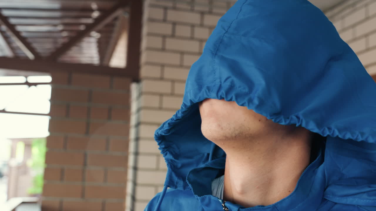 雨を避けて軒下でフードを被る若者、天候を確認するために立ち止まる都会のアスリート、ジャケットを調整する通勤者、練習の準備をするフットボール選手、フードで顔を覆った覆面姿、静寂。