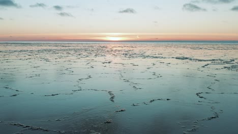 drone flying over calm sea with melted ice at the surface at sunset, sunrise