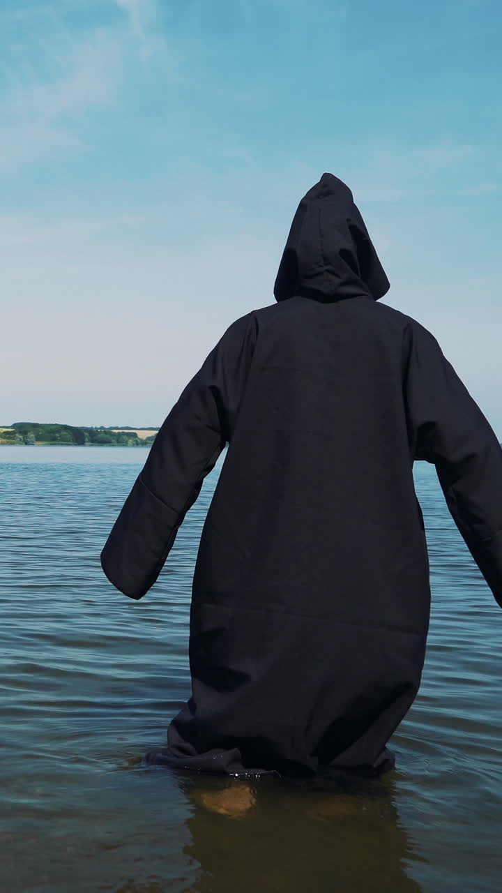 Terrible witch in black mantle in the water outdoor.. Vertical video