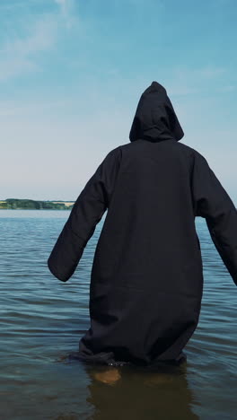 terrible witch in black mantle in the water outdoor.. vertical video