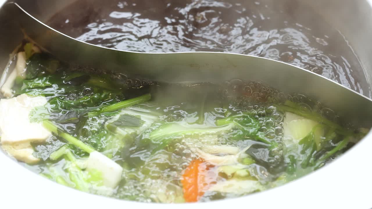 Thin beef slice cooked in steaming dual broth hotpot with assorted vegetables, overhead view
