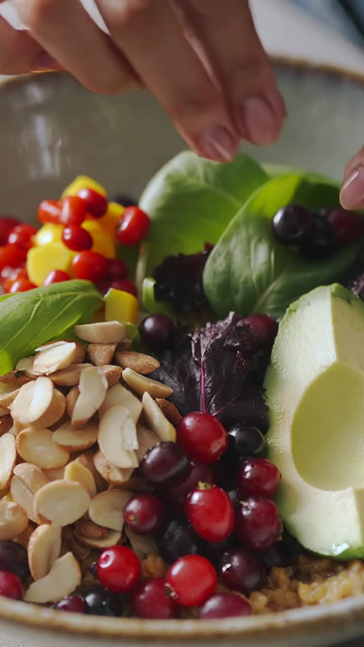 Vertical video: Opening cook's hands arranging almonds berries avocado in bowl on kitchen counter