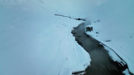 Steam-Rising-From-The-Geothermal-Hot-River-At-Reykjadalur,-Iceland-During-Winter---aerial-drone-shot