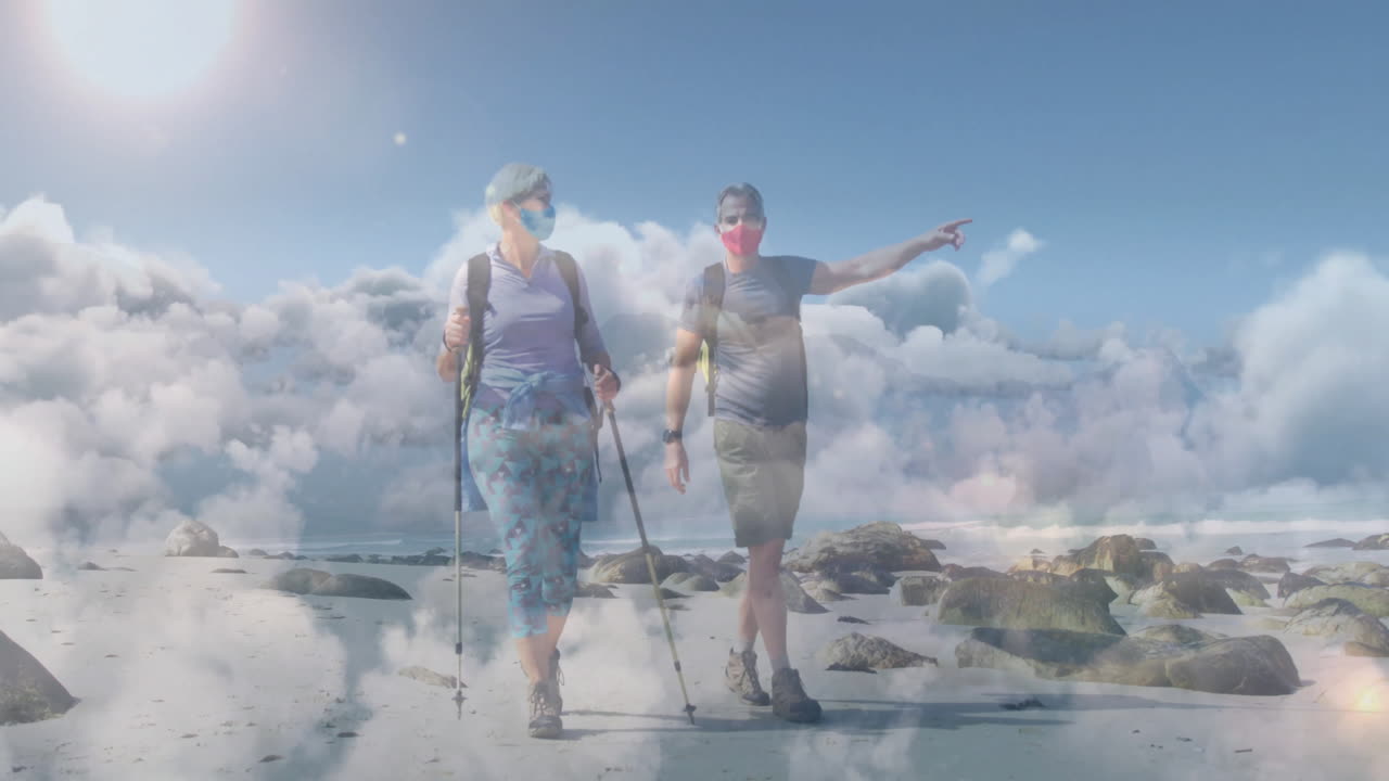 Couple hiking beach wearing masks and using trekking poles depicting health with cloud overlay