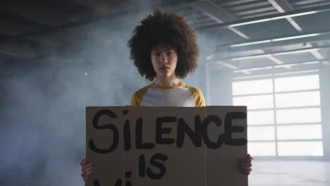 Portrait-of-african-american-woman-holding-protest-placard-in-empty-parking-garage-in-empty-parking-